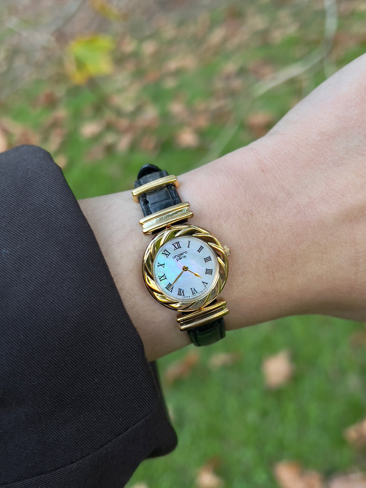 Seiko x Ungaro gold watch with a white face on a wrist against a blurred natural background