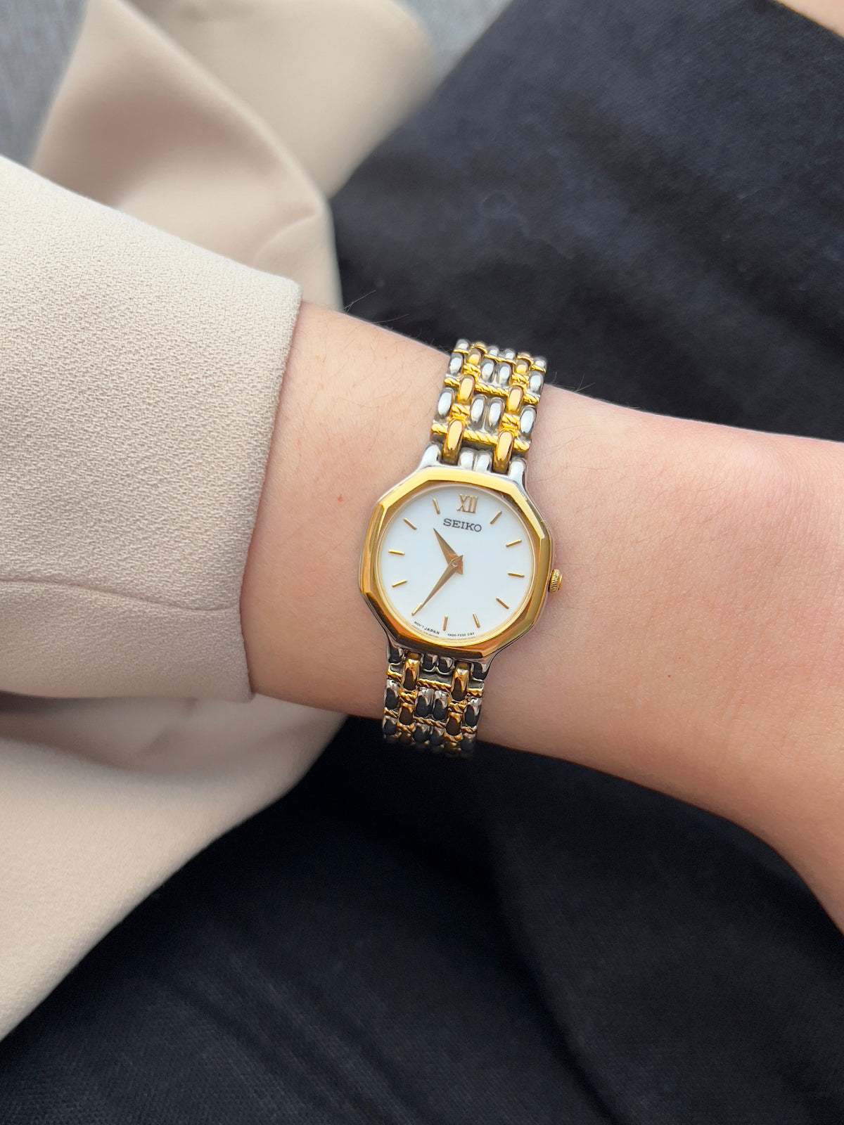 Gold and silver watch on a wrist with a neutral background