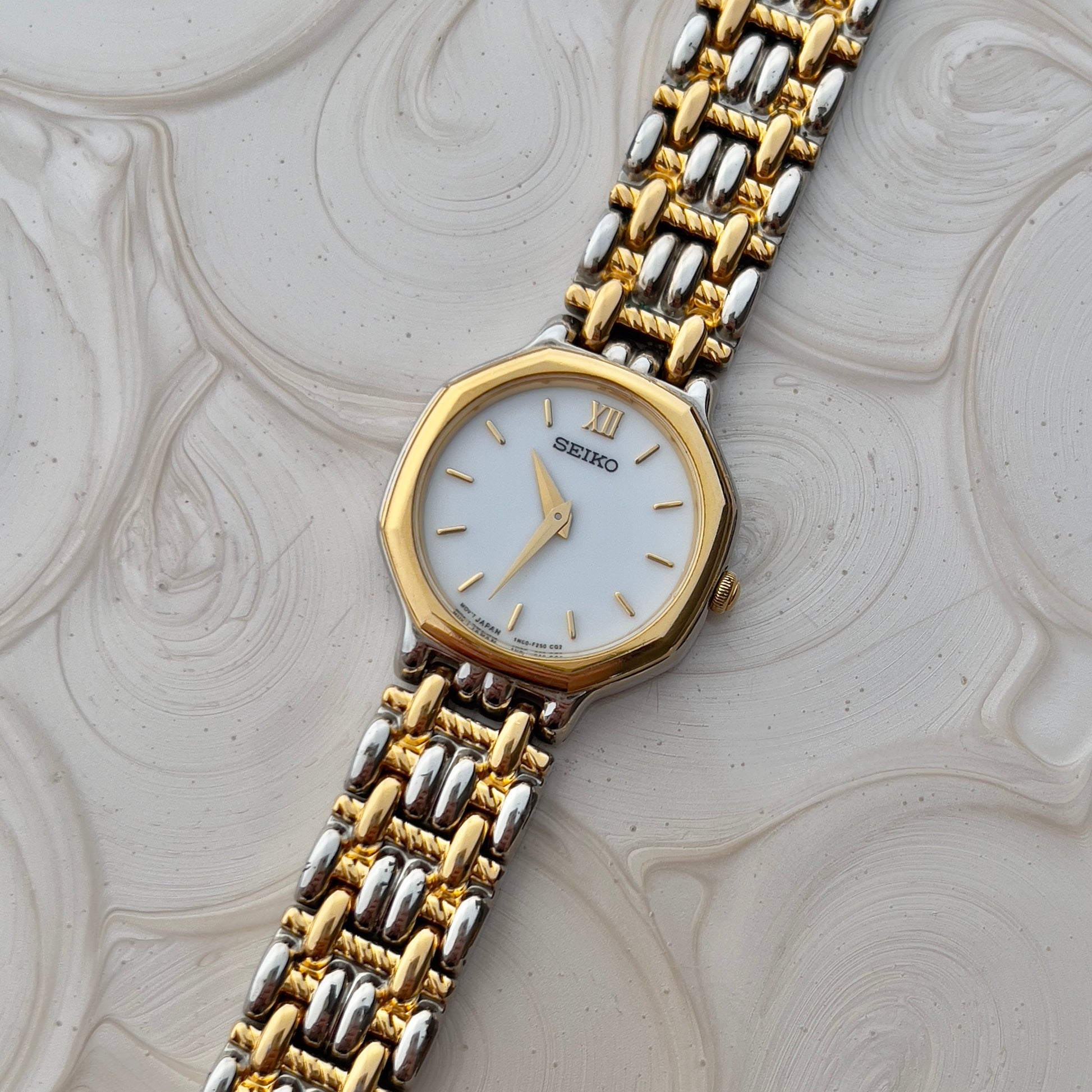 Seiko two-tone gold and silver watch on a textured beige background