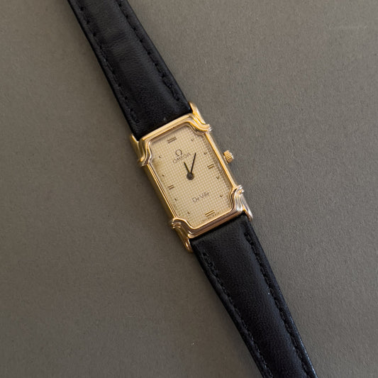 Gold Omega De Ville watch with black leather strap on a gray background
