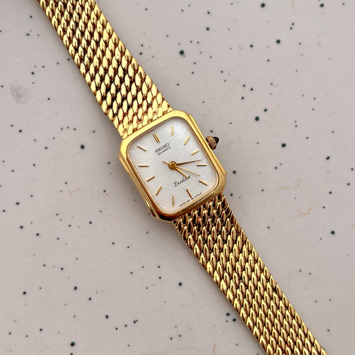 Gold wristwatch with a white face on a speckled gray background