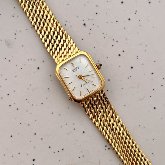 Gold wristwatch with a white face on a speckled gray background