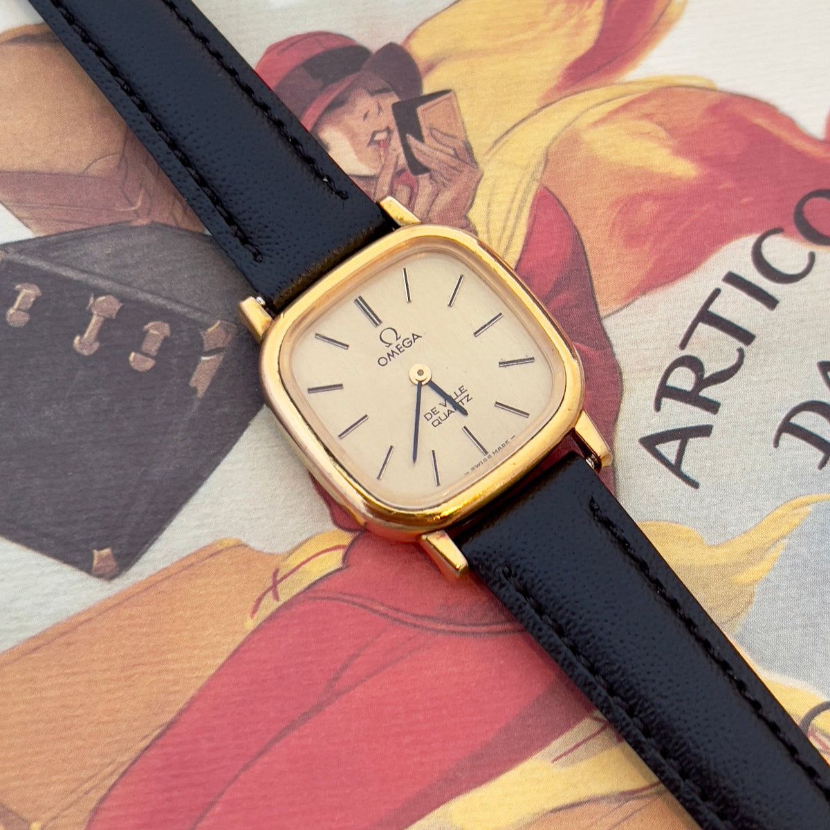 Gold Omega watch with black strap on vintage magazine background