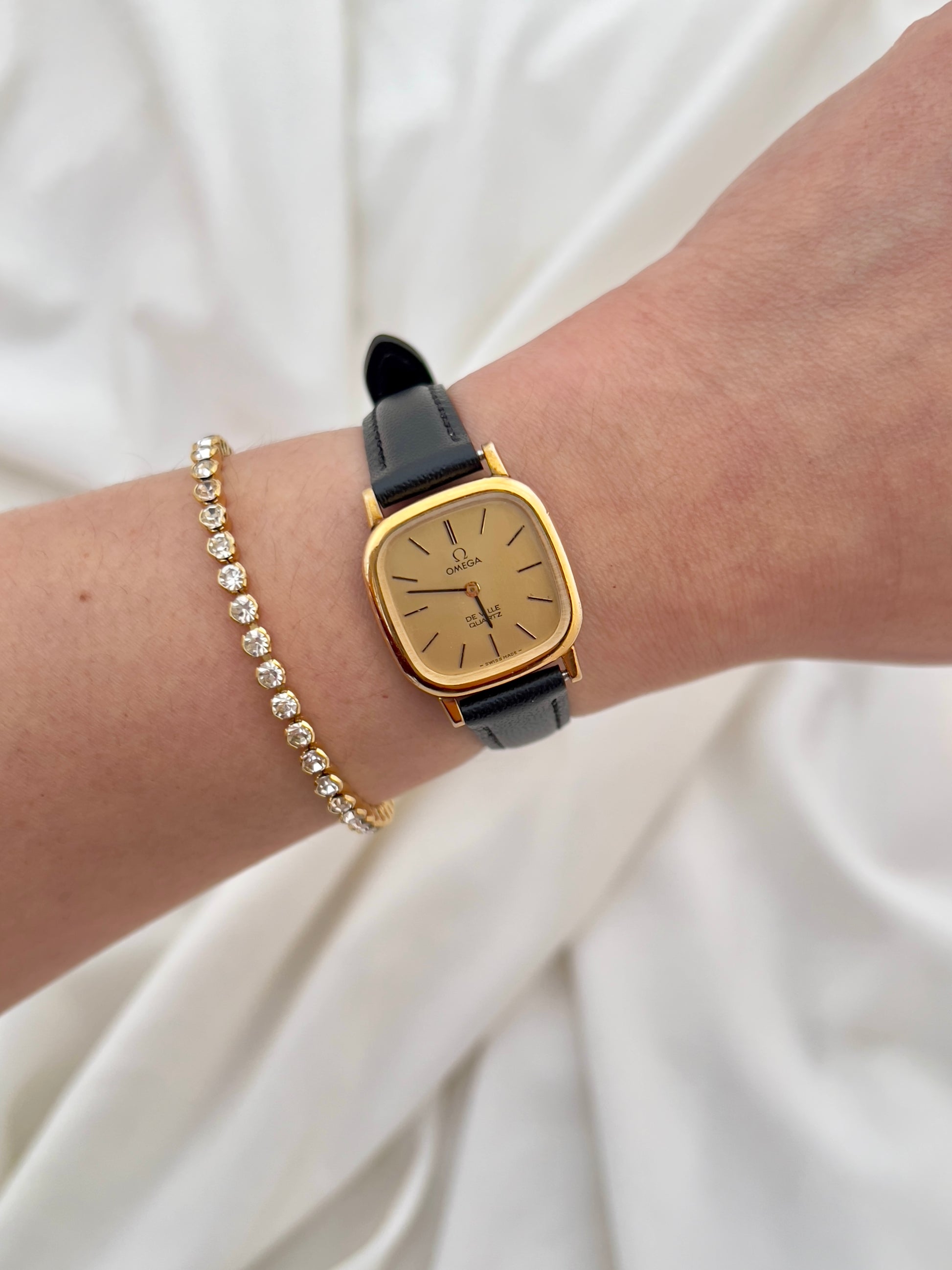 Omega Gold watch with black strap on a wrist against a white background
