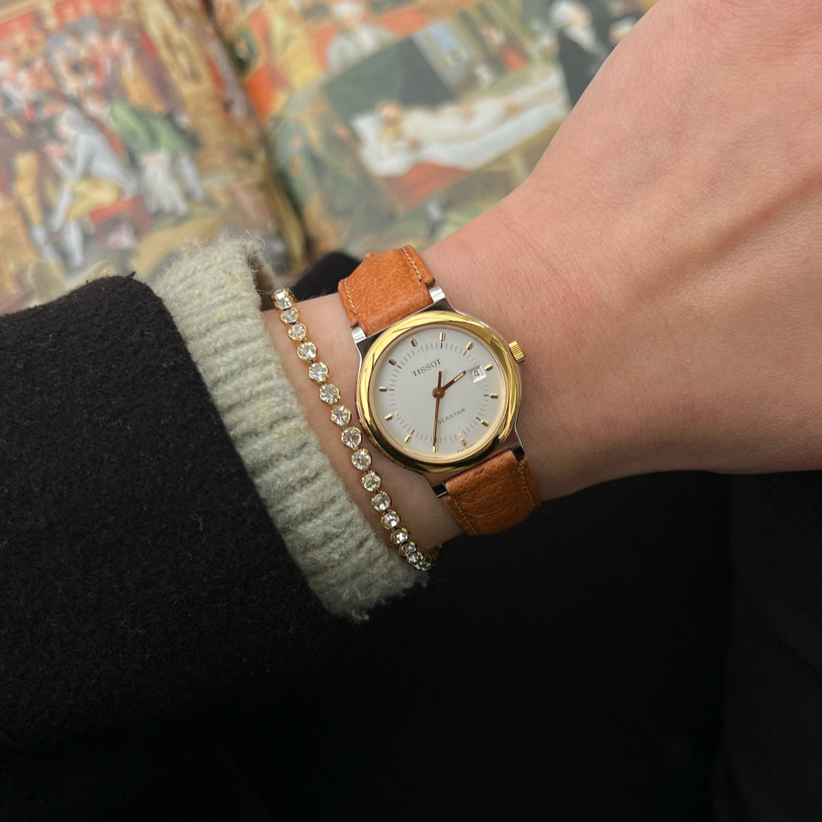Tissot gold watch with a brown leather strap on a patterned surface
