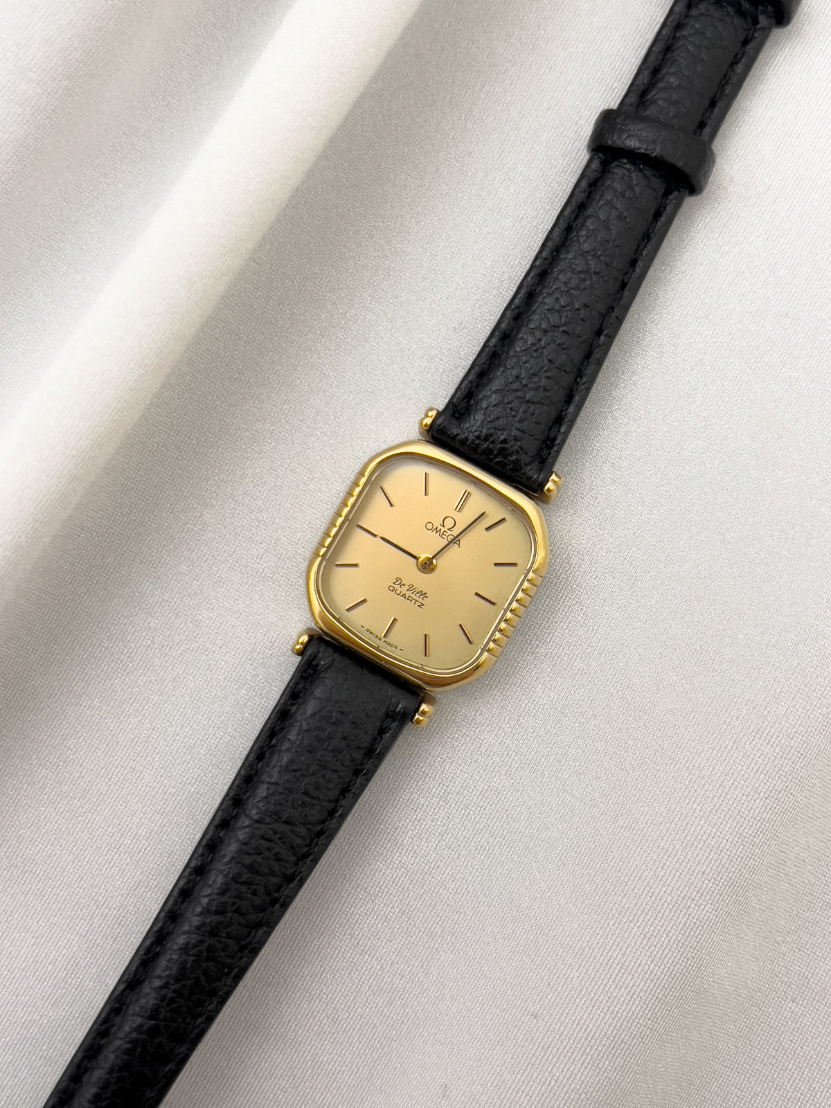 Vintage Omega gold wristwatch with black leather strap on a light gray background