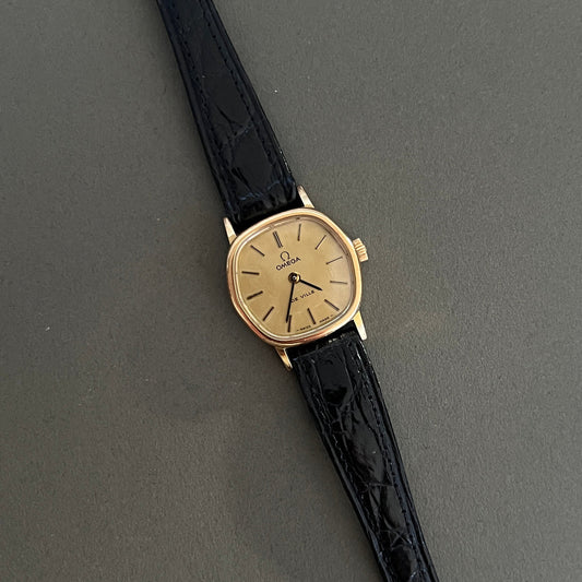 Vintage Omega De Ville gold watch with black strap on a gray background