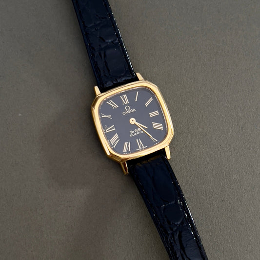 Omega Wristwatch with black strap and gold case on a gray background