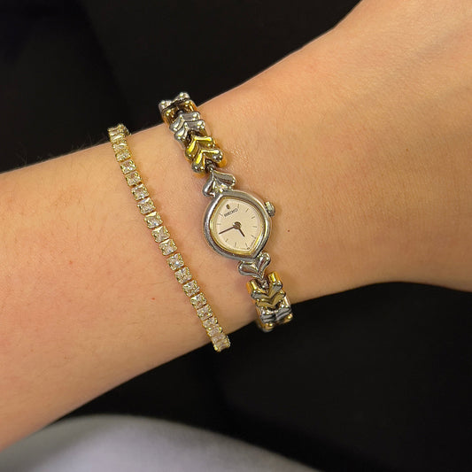 Wrist wearing a silver watch with gold accents on a dark background