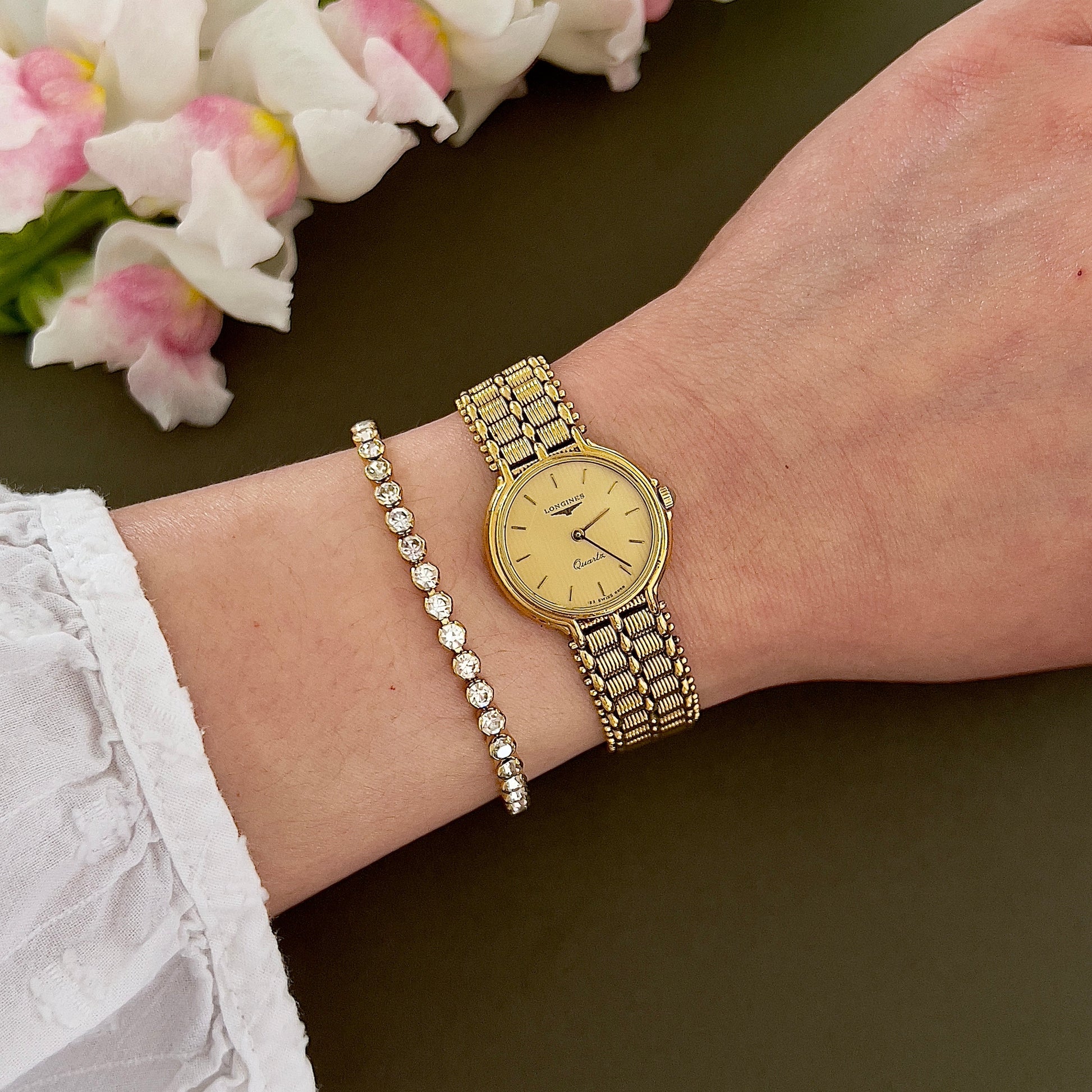 Gold Longines Ladies' watch and bracelet on a wrist with flowers in the background