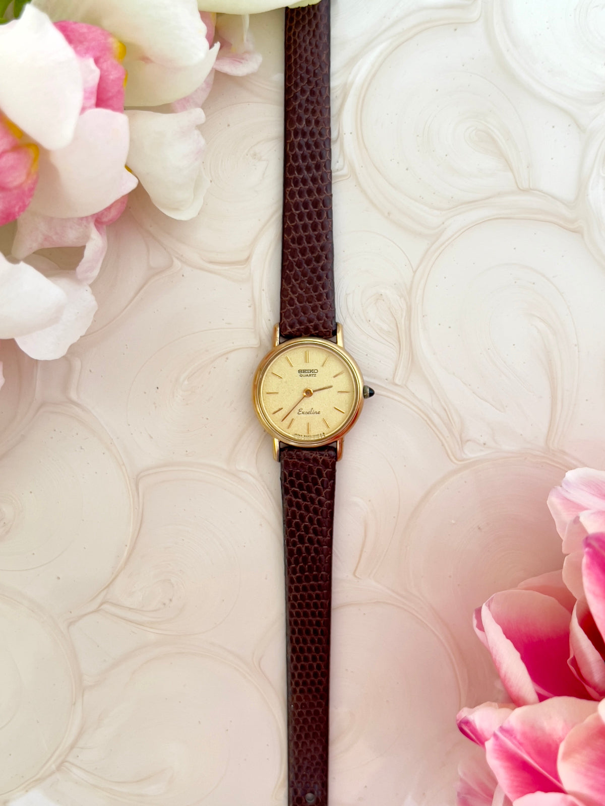 Gold watch with brown strap on a textured surface with pink flowers