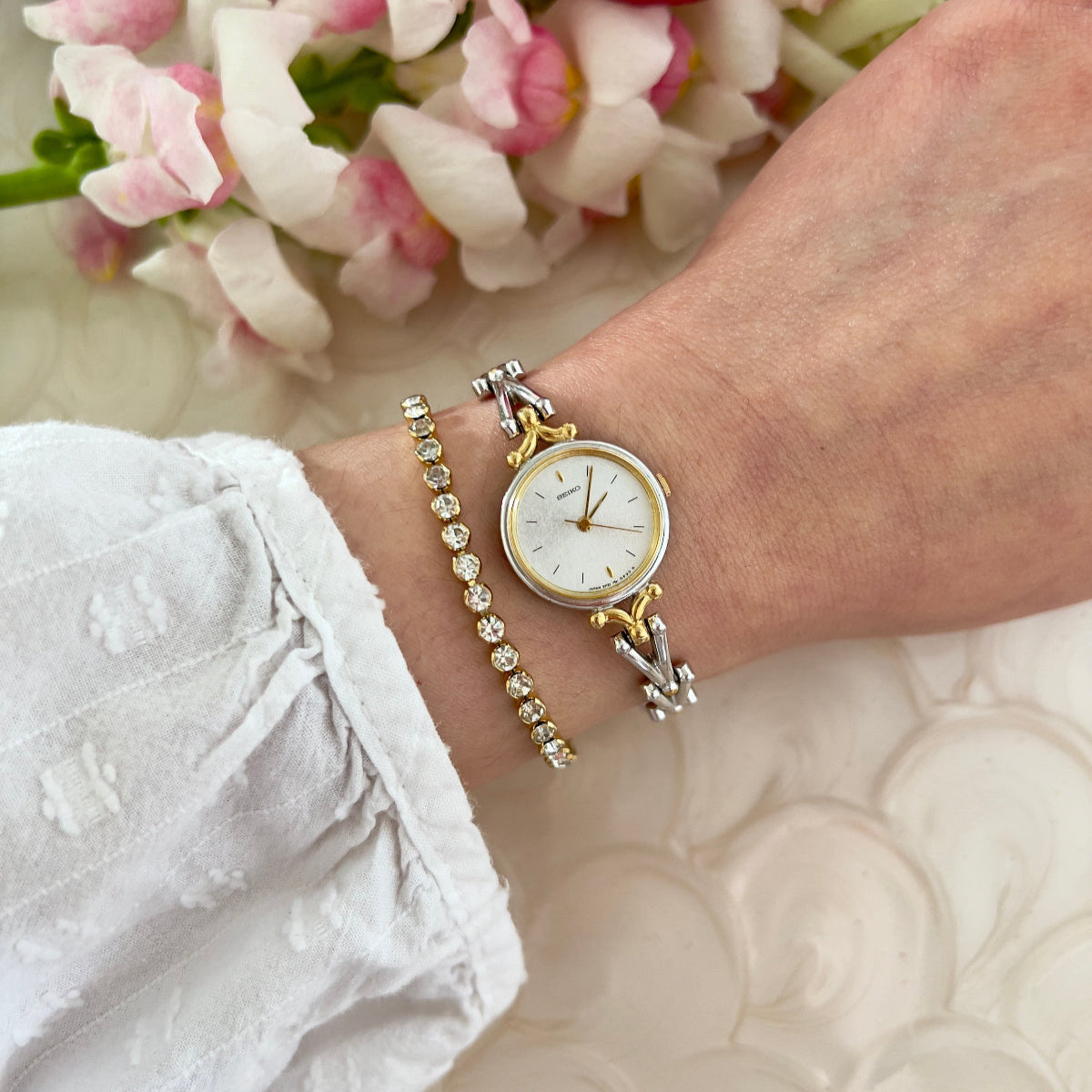 Seiko gold watch and bracelet on a wrist with flowers in the background