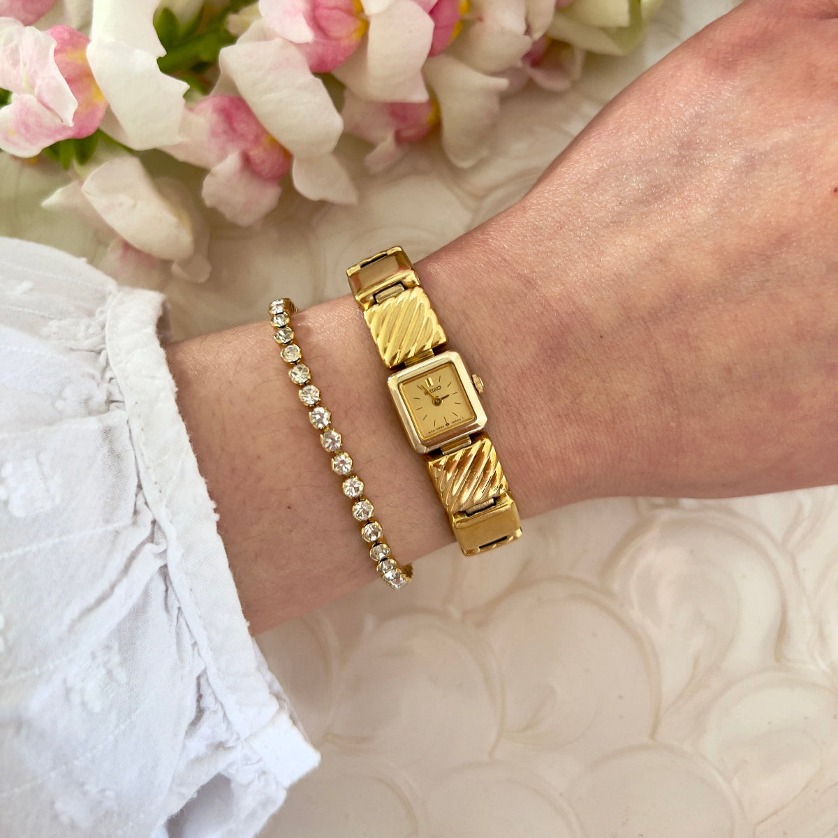 Gold Seiko bracelet watch on a wrist with flowers in the background