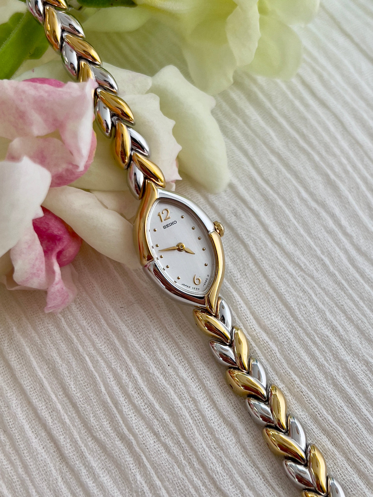 Seiko gold and silver braided watch on a textured surface with flowers