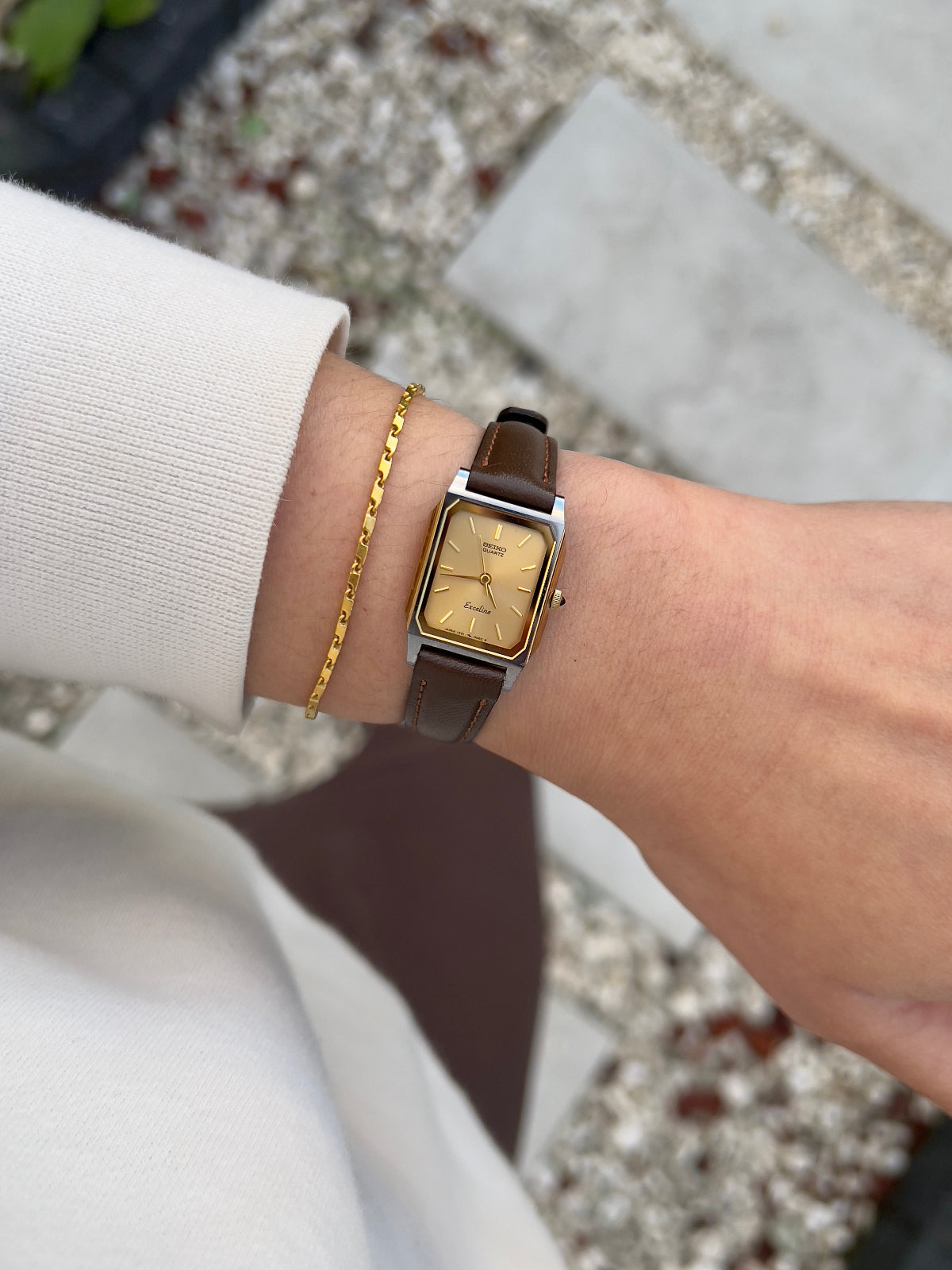Vintage Seiko Exceline ladies gold tank watch with double-framed rectangular case and brown leather strap, styled on herringbone tweed fabric.