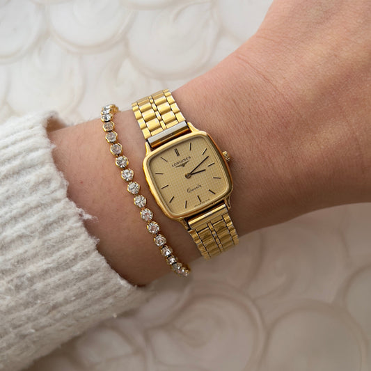 Vintage Longines gold square watch with champagne dial and waffle texture on wrist, paired with crystal bracelet.