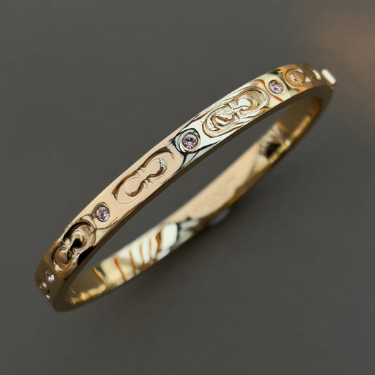 Coach Gold bracelet with intricate designs and small gemstones on a dark background