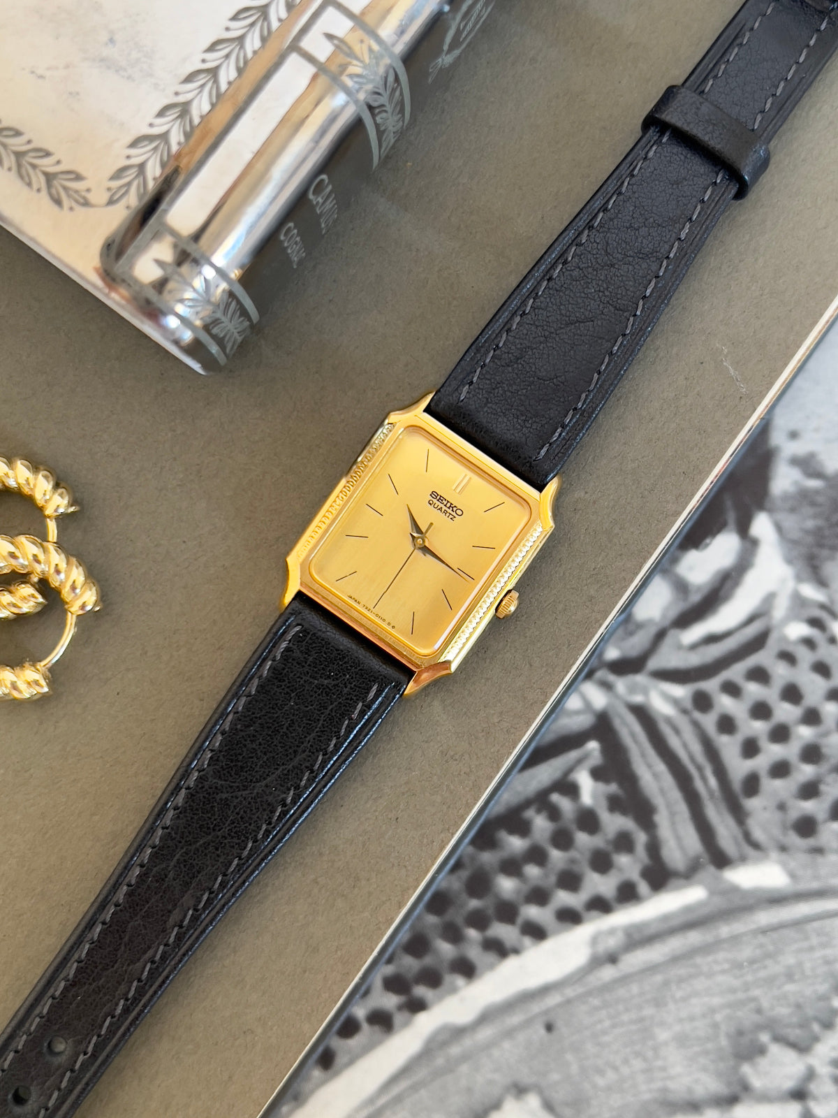 Gold watch with black leather strap on a textured surface