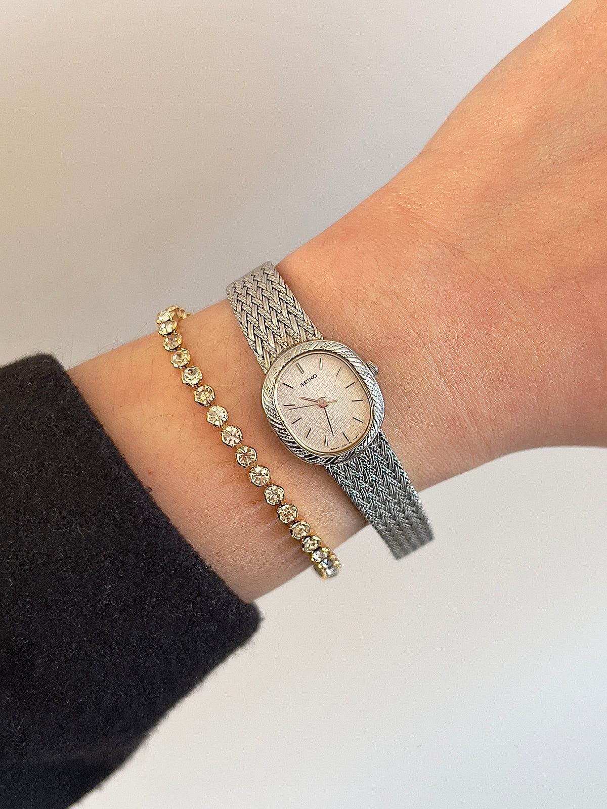 Wrist wearing a silver watch and gold bracelet on a neutral background