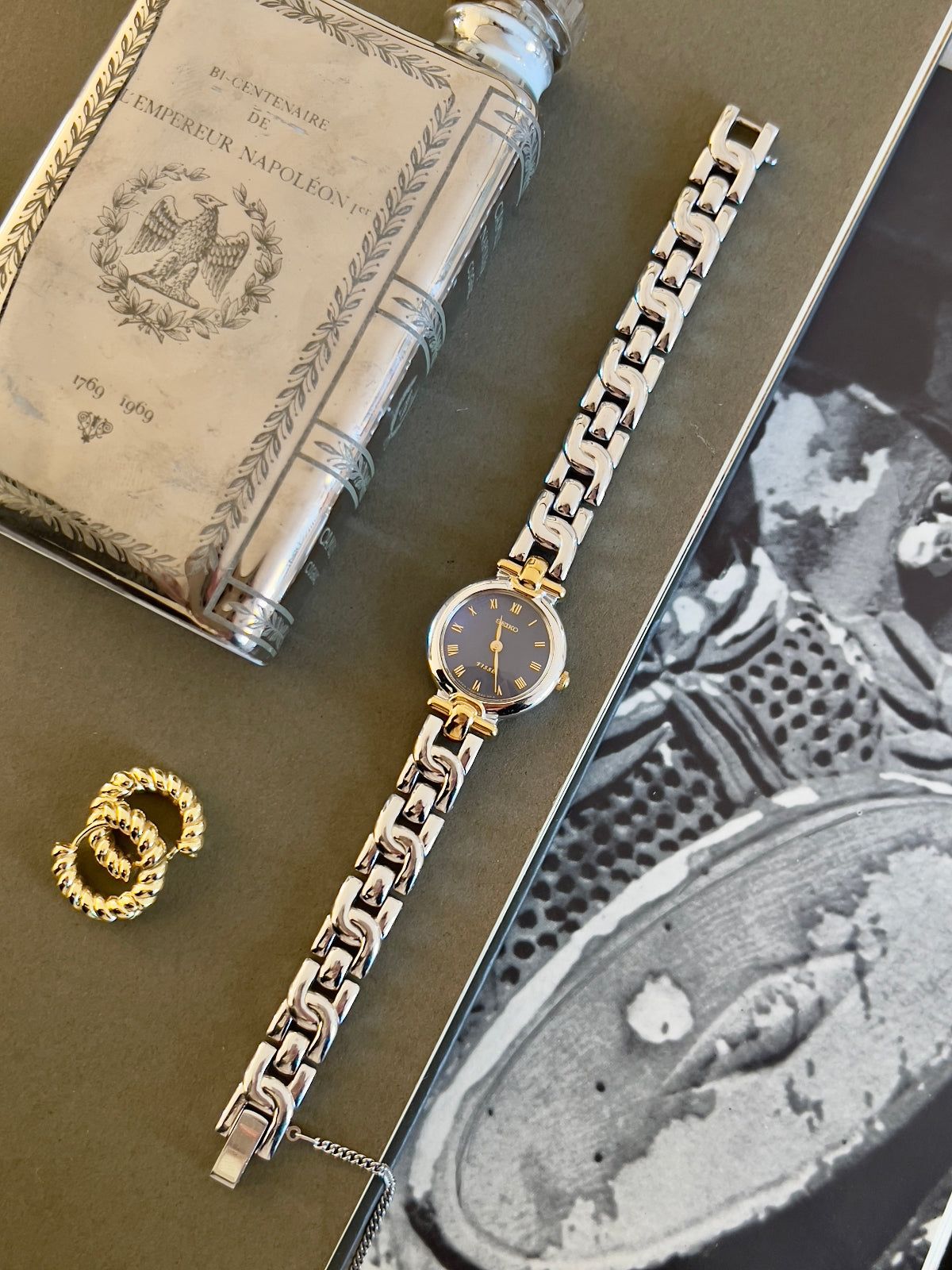Seiko gold and silver woman's watch on a textured surface with a book and black and white photo.