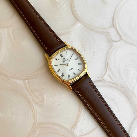 Omega vintage watch with brown leather strap and gold case on a textured beige background