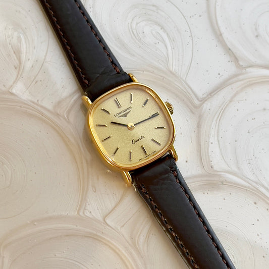 Gold wristwatch with a brown leather strap on a textured white background