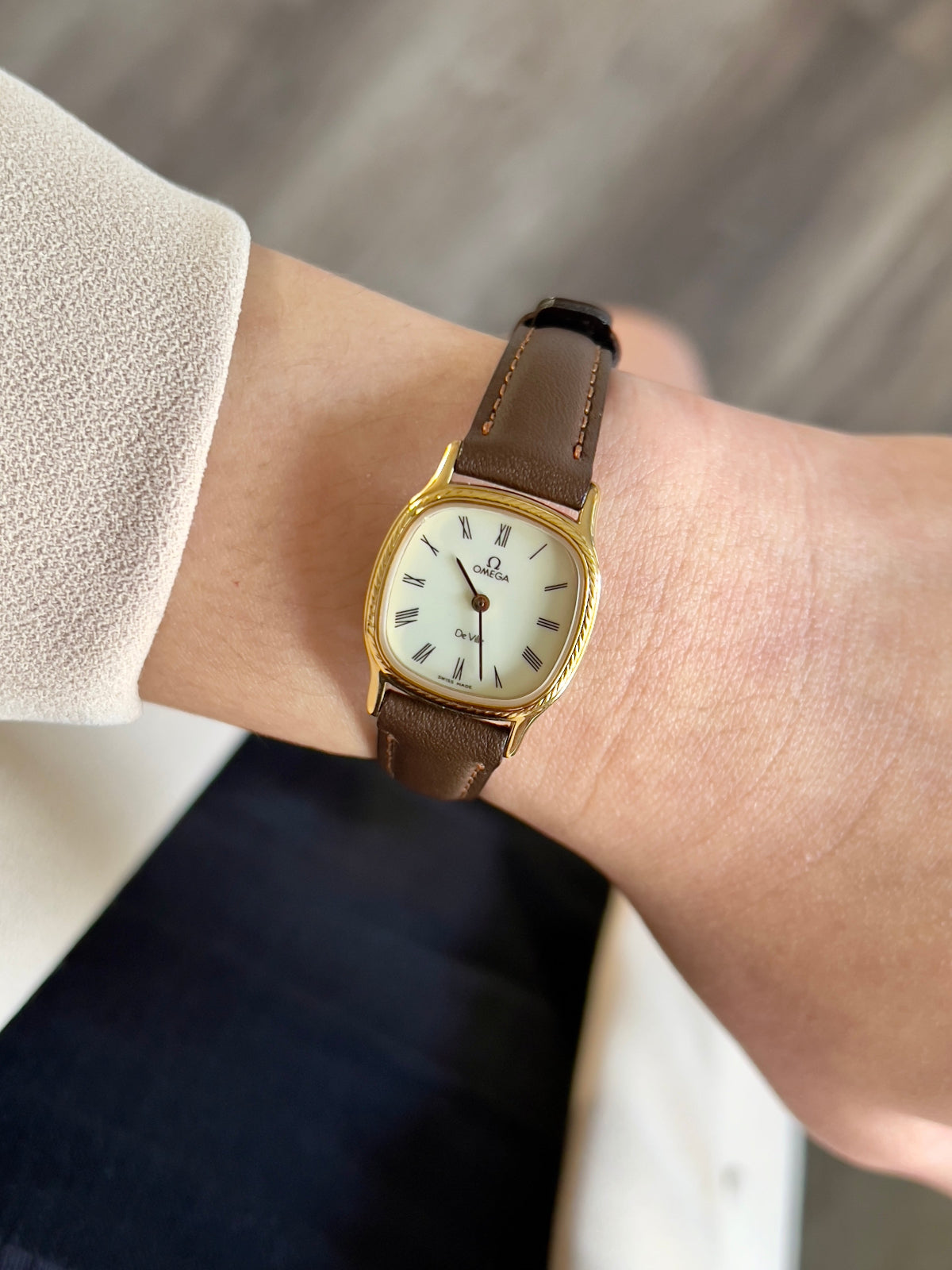 Omega Gold luxurious woman's watch with a brown leather strap on a wrist against a neutral background