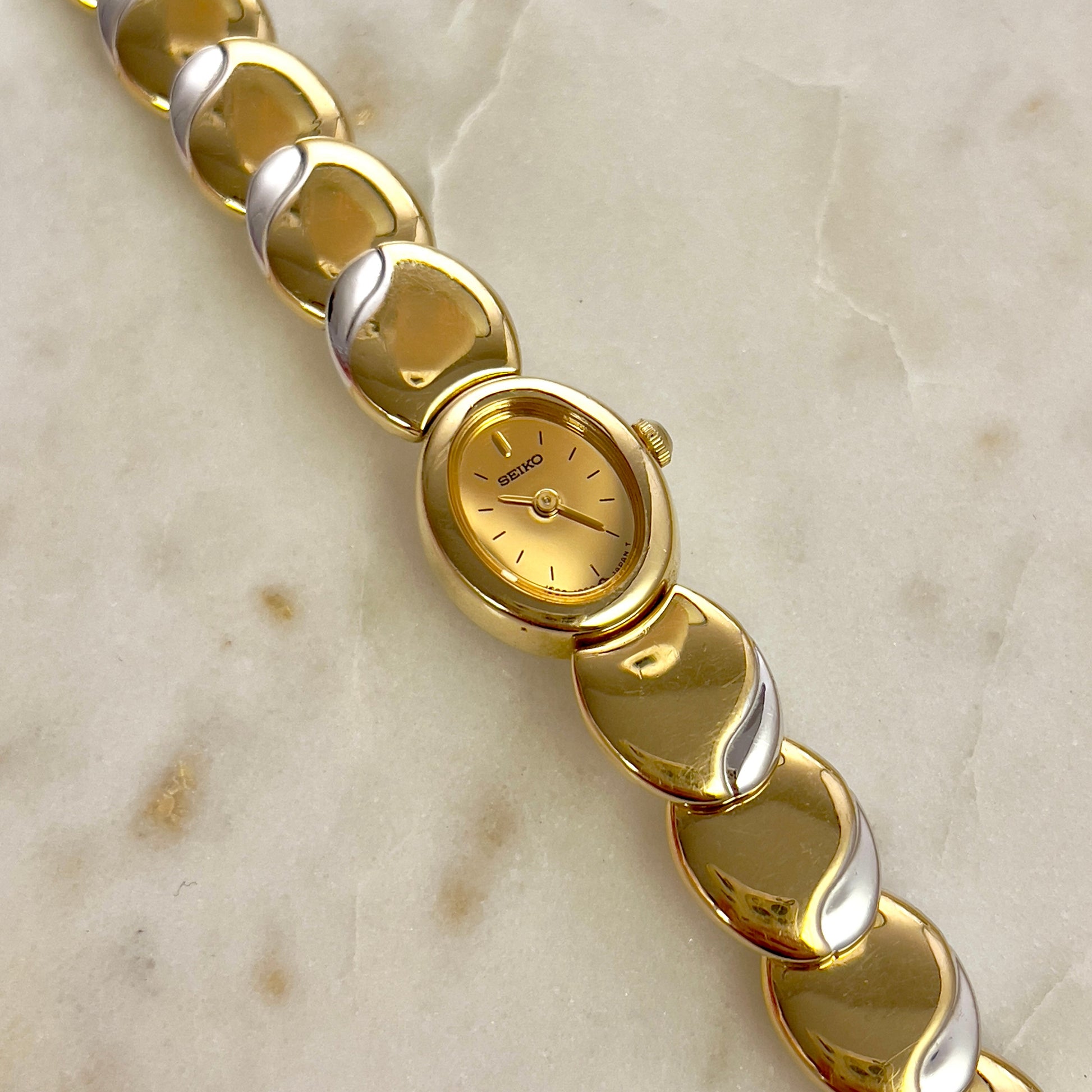 Seiko gold and silver bracelet with a watch face on a marble surface