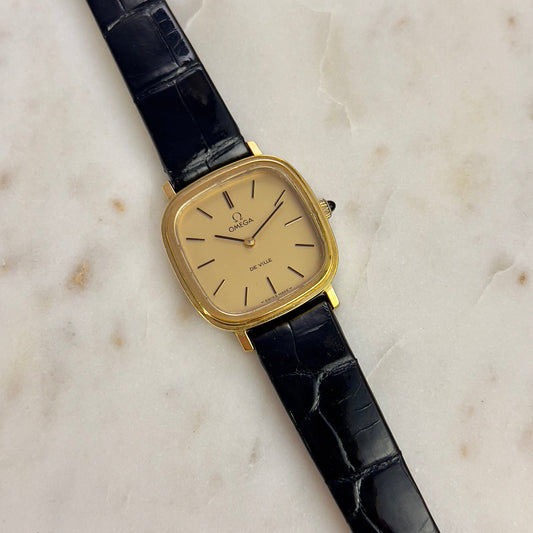 Vintage Omega ladies watch with black strap and gold case on a marble surface