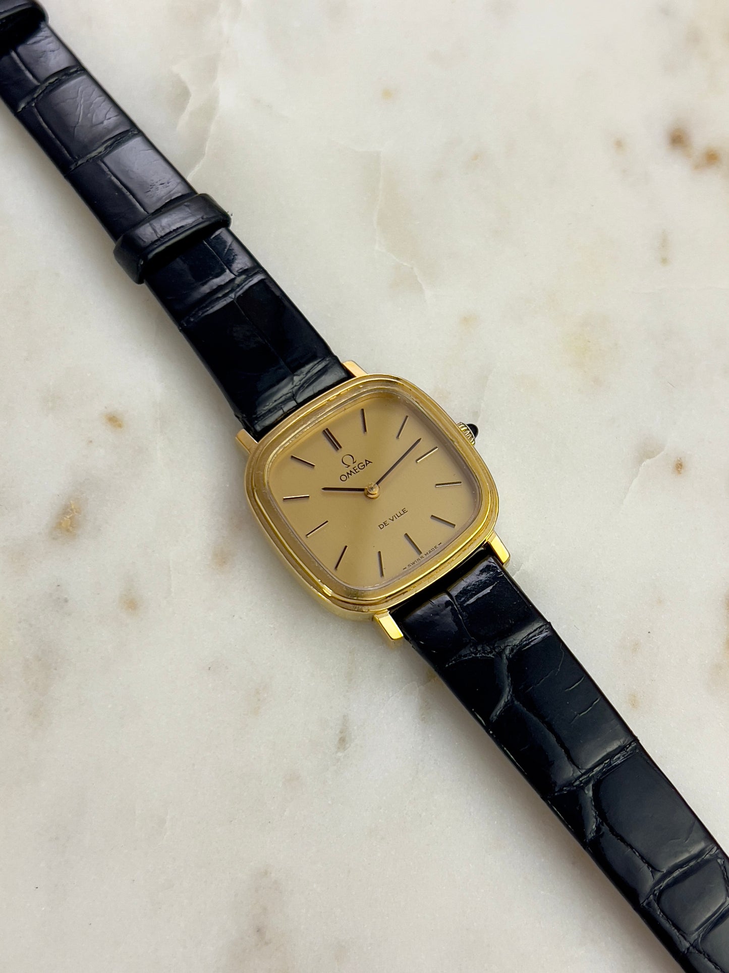 Vintage Omega watch with black leather strap on a marble surface