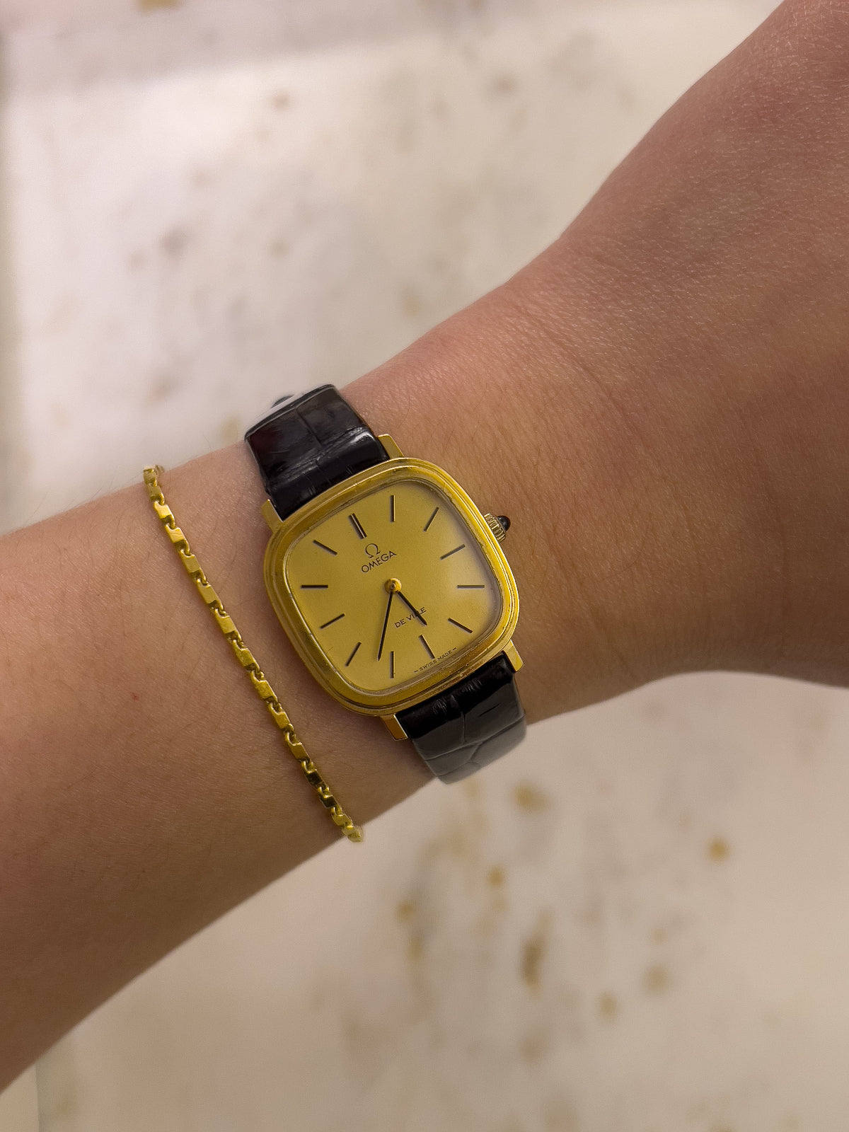 Yellow watch with black strap on a wrist against a neutral background