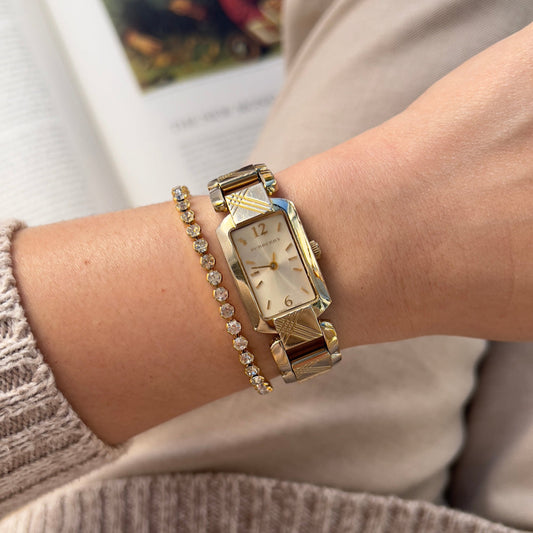 Burberry gold watch and bracelet on a wrist with a blurred background