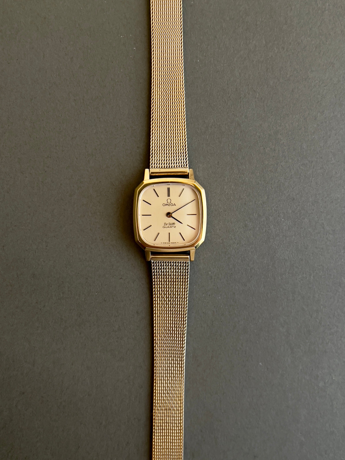 Omega gold watch with mesh band on a gray background