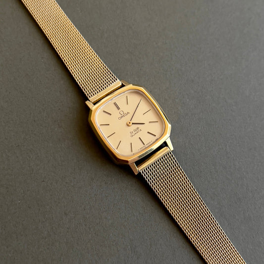 Omega Gold women's watch with mesh strap on a dark gray background