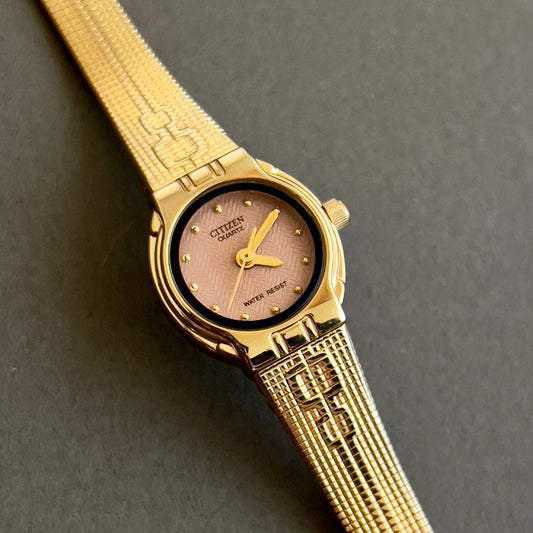Citizen gold wristwatch with a detailed band on a gray background