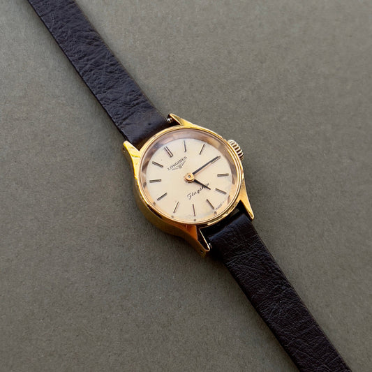 Vintage watch with gold case and black leather strap on a gray background