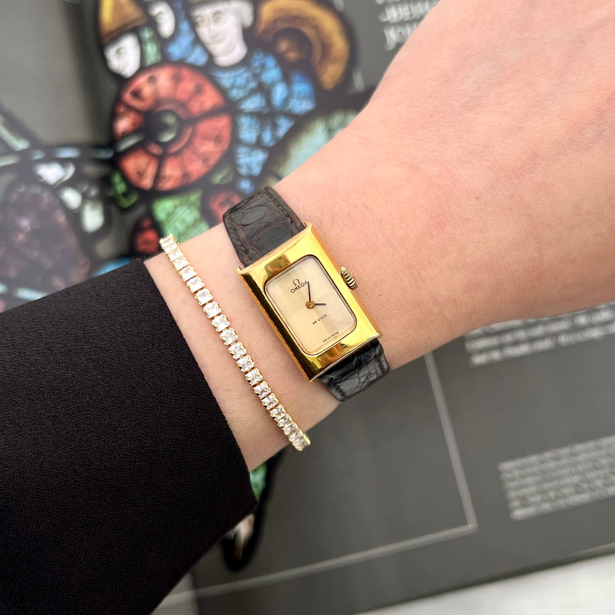 Omega Ladies Gold watch on a wrist with a stained glass window in the background