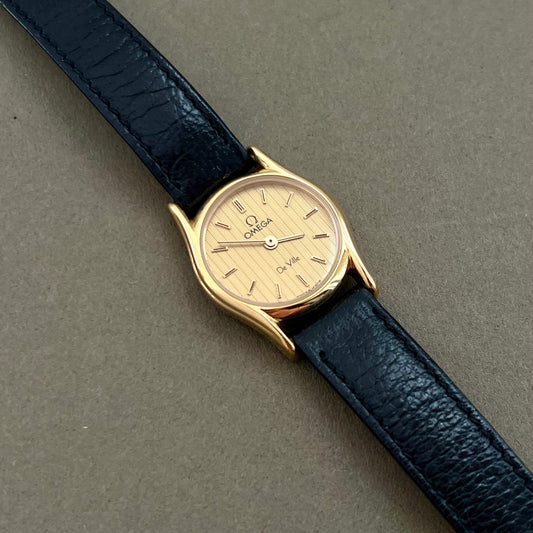 Omega De Ville ladies gold rectangular watch with champagne textured dial and black leather strap on wrist
