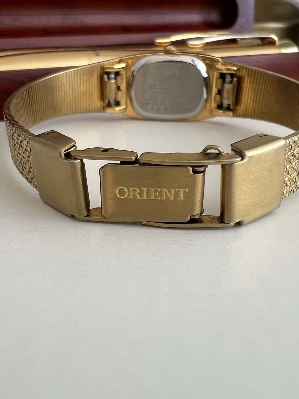 Orient signed folding clasp on the gold tone mesh bracelet, with the caseback and bracelet underside visible.