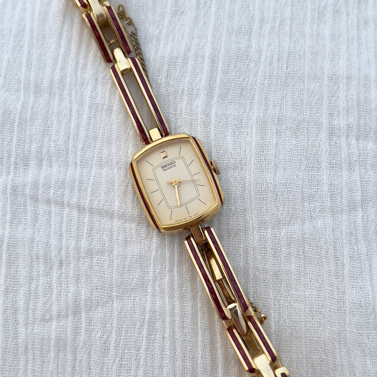 Seiko ladies gold bracelet watch with ruby enamel detailing and champagne dial worn on wrist beside diamond bracelet