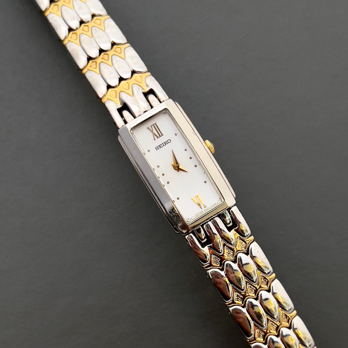 Seiko ladies two tone bracelet watch with white dial, featuring an elegant rectangular case and sculpted gold and silver bracelet that glows like jewellery.