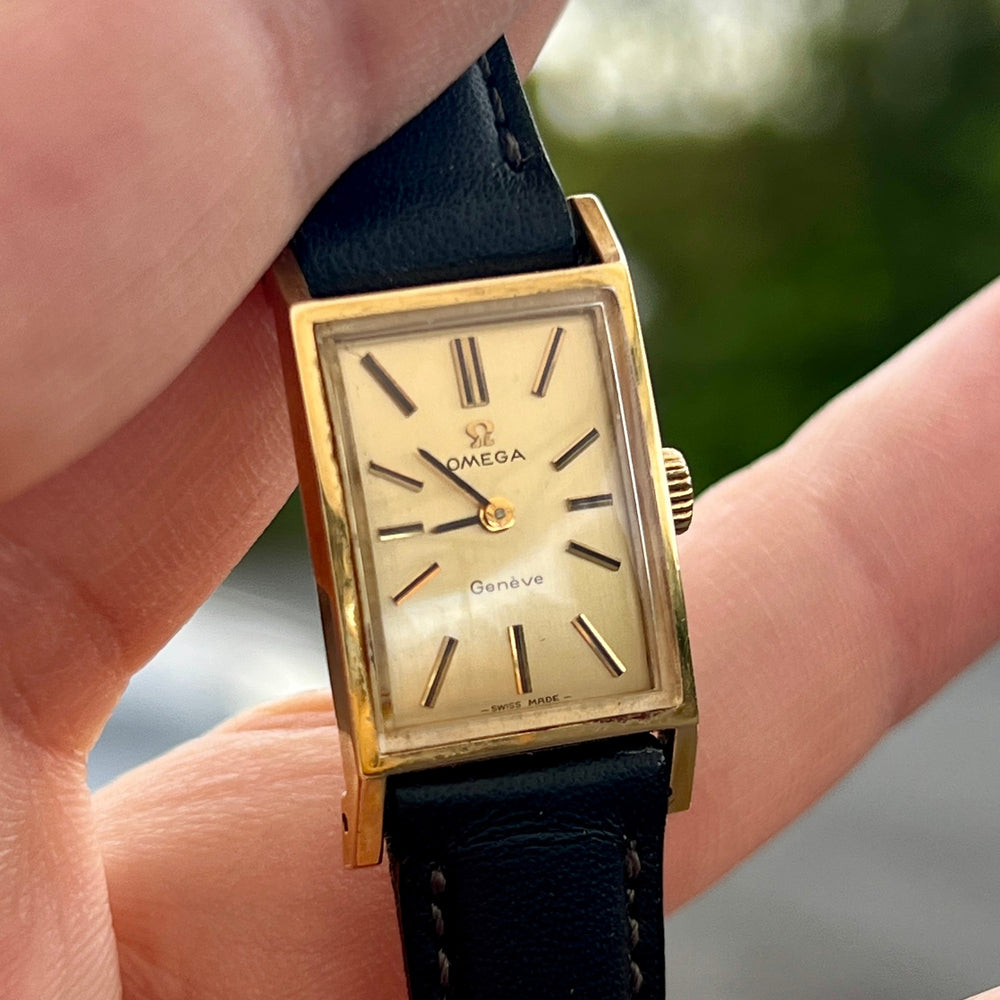 Close view of a rectangular vintage Omega Genève women’s watch with a gold-tone case and black leather strap