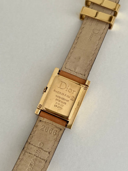 Gold Dior Malice watch with beige strap on a light gray background