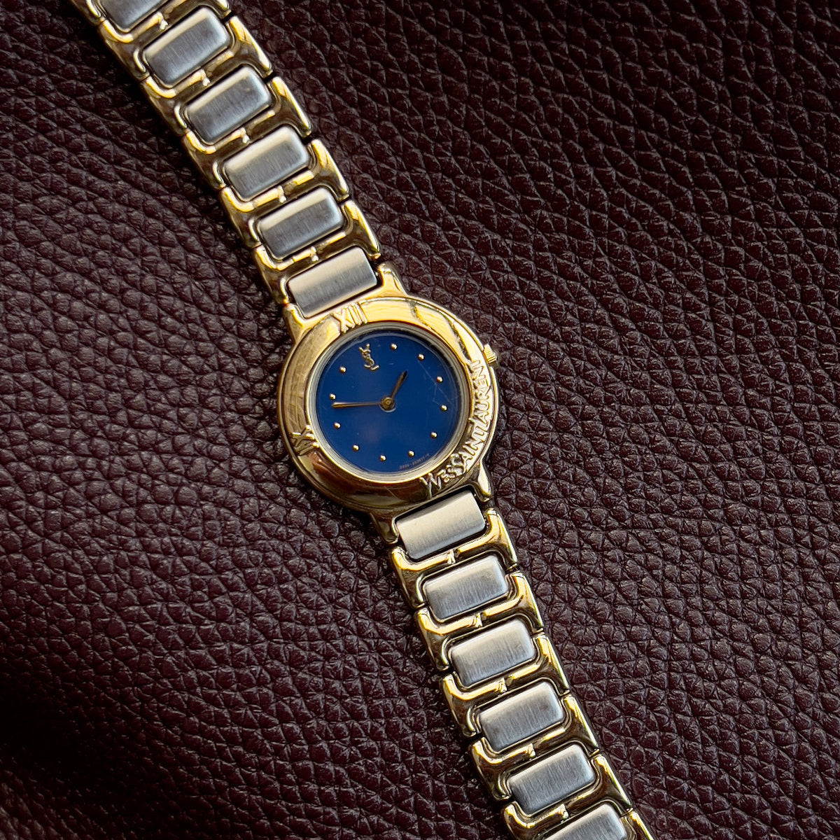 YSL Gold and silver watch with blue face on a brown textured background