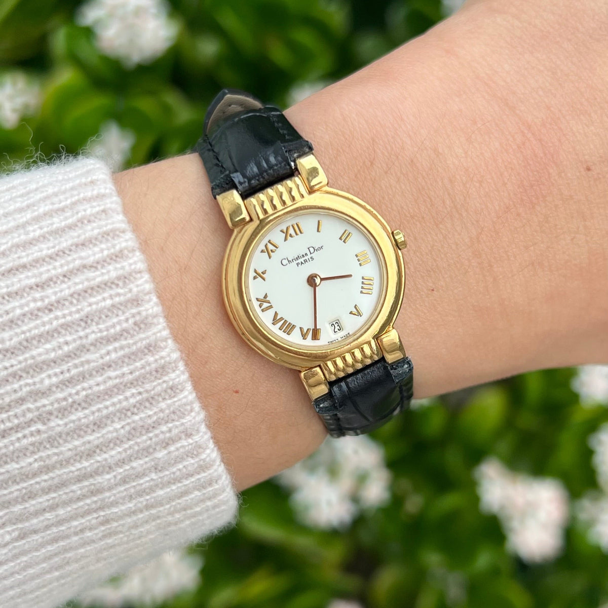 Gold Christian Dior women's watch with a white Roman numeral dial worn against a floral background