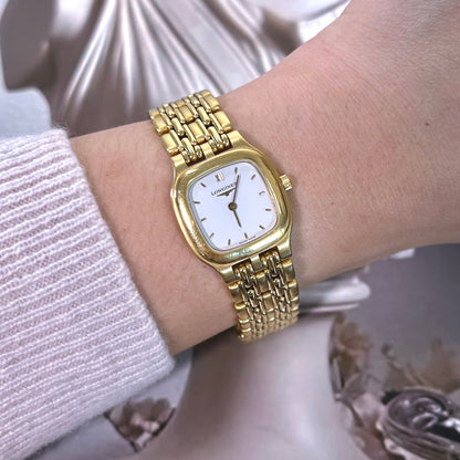 Gold Longines wristwatch on a person's wrist with a classical sculpture in the background