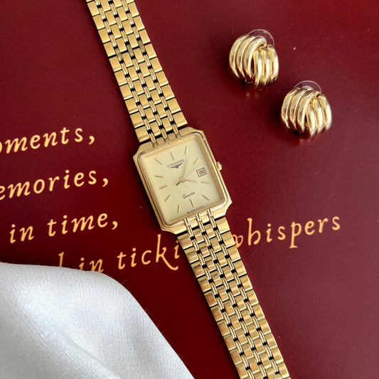 Gold Longines Flagship watch and earrings on a textured red surface with text.