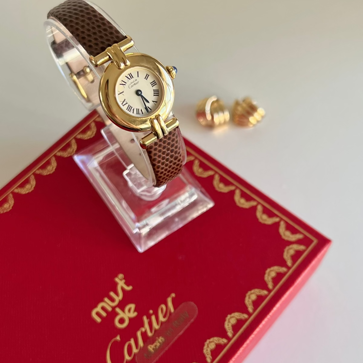 Gold Must de Cartier Colisse watch with brown strap on a display stand with Cartier box in the background
