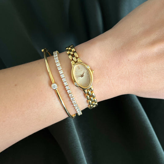 Gold watch and bracelets on a wrist against a black background