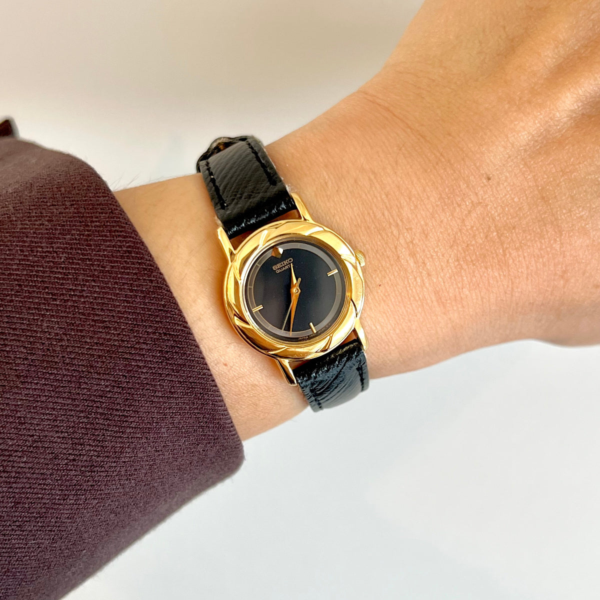 Gold Seiko Women's watch with black strap on a wrist against a neutral background